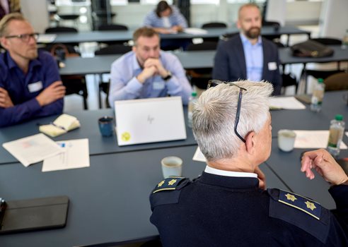 2026 05 07 Deltagere Sidder Til Møde I Et Mødelokale, Mens En Uniformeret Deltager Fra Beredskabsmyndighed Deltager I Diskussionen Recilienscenter Danmark