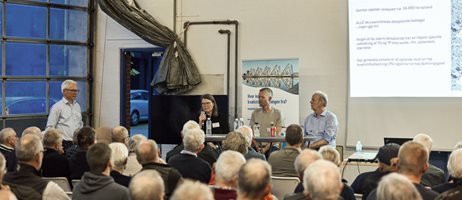 2026 09 30 Deltagere Sidder Tæt I Vejle Spildevands Garage, En Kvinde Taler I Mikrofon Ved Et Vejle Spildevand